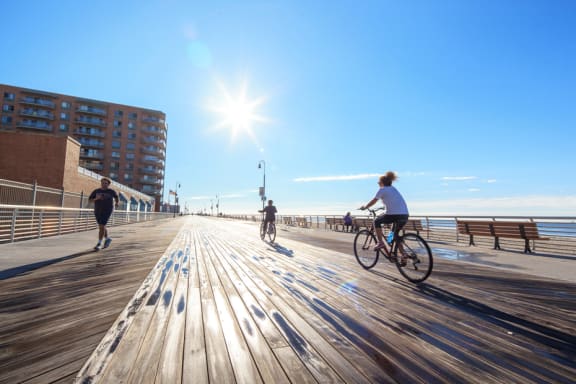 A sunny day at the beach with people jogging and biking on the boardwalk at 10 West Apartments, Long Beach, New York