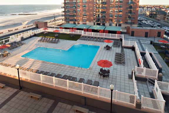 A large pool with a table and chairs is surrounded by a white fence at 10 West Apartments, Long Beach, 11561