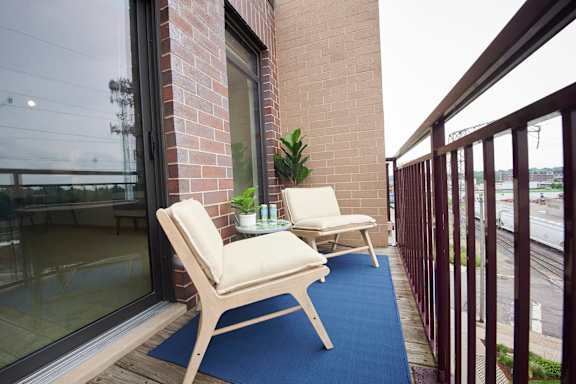 A balcony with a blue rug and two chairs.