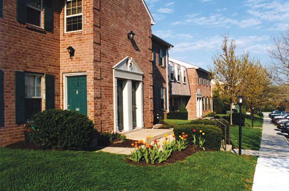 Exterior view of a red brick building with a white door, green shutters, and surrounding greenery at New Kent Apartments in West Chester, PA