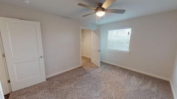 Bedroom with a ceiling fan and carpeted floor.