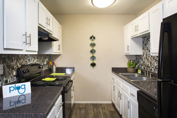 Kitchen in Fifteen 50 apartments in Las Vegas with black appliances, white cabinets, and black granite-style countertops