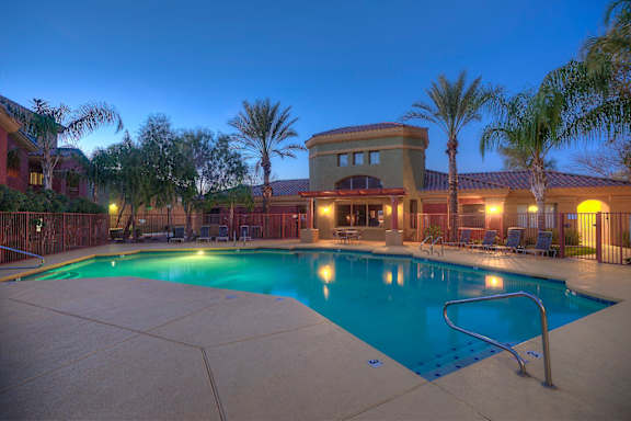 A pool surrounded by palm trees and a building in the background at San Miguel Apartments, Mesa, Arizona