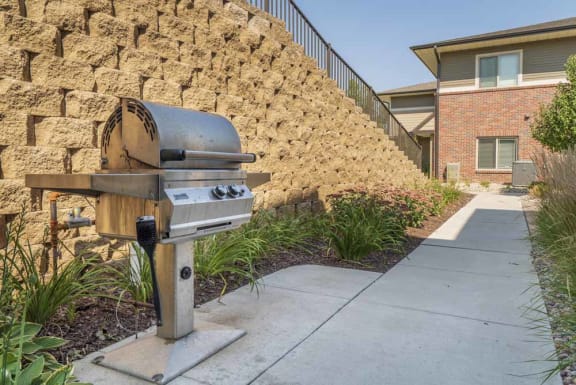 A barbecue grill is in front of a stone wall and a house.