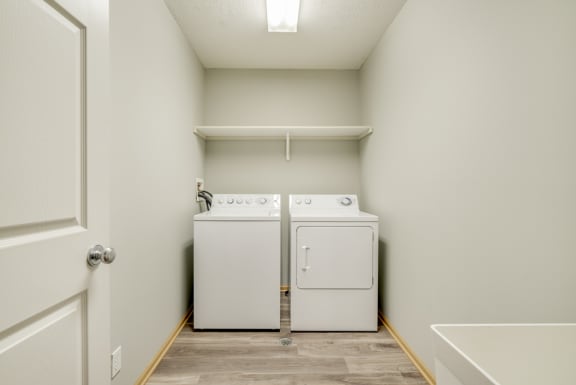 Laundry room with white washer and dryer and empty shelf above them