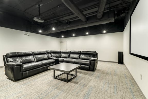 A black leather couch and table in a room with a white wall and carpet.