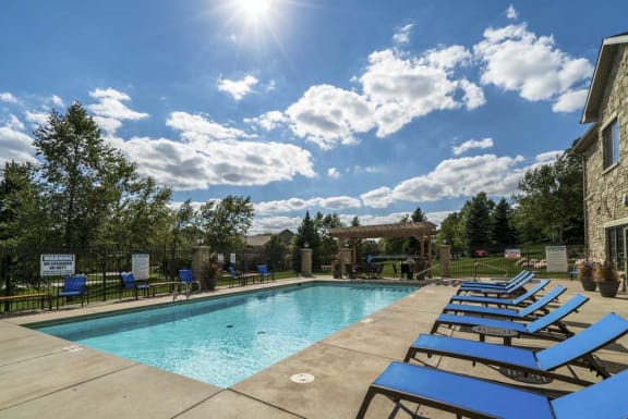 A sunny day at the pool with blue lounge chairs and a clear sky.