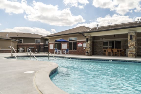 A swimming pool in front of a building with a blue umbrella.