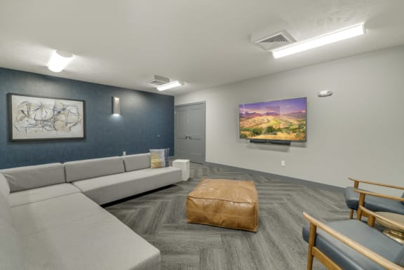 A room with a grey couch, a brown ottoman, and a painting on the wall.