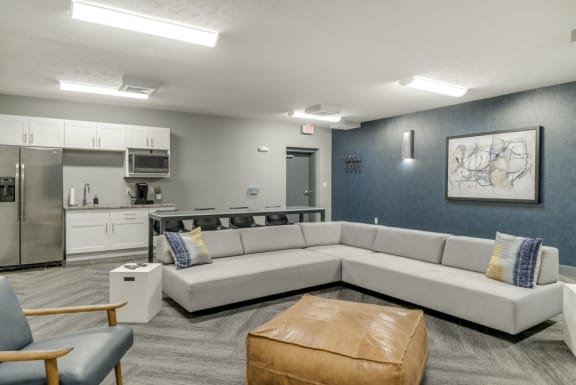 A modern kitchen and living room area with a grey sofa and a brown leather ottoman.