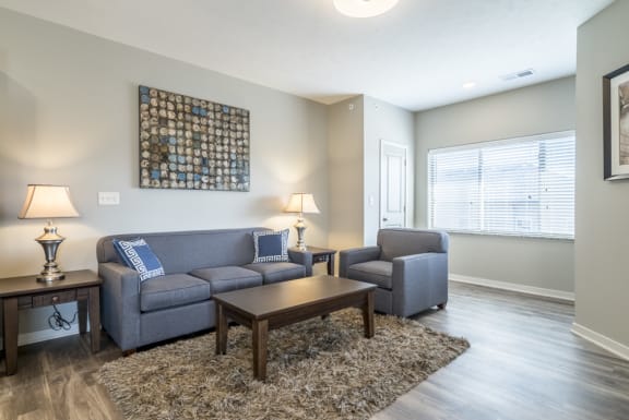 A living room with a grey couch, a chair, and a table with a lamp on it.