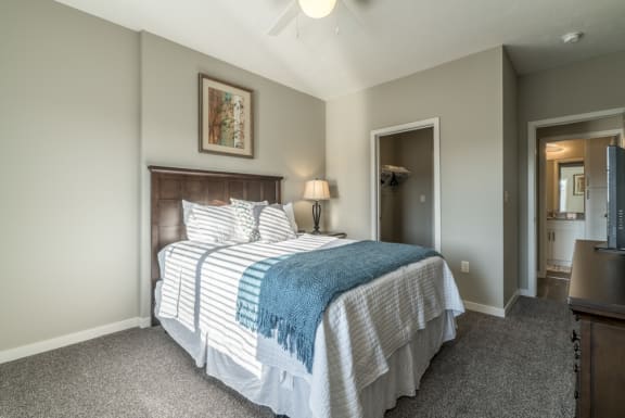 A bedroom with a bed, a ceiling fan, and a painting on the wall.