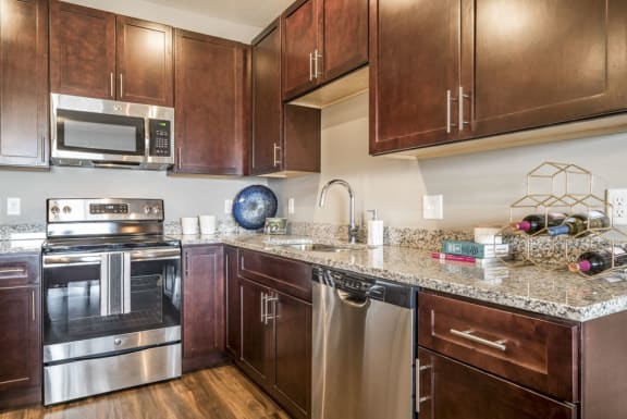 Open kitchen with granite countertops and dark brown cabinets at 360 at Jordan West in West Des Moines, IA