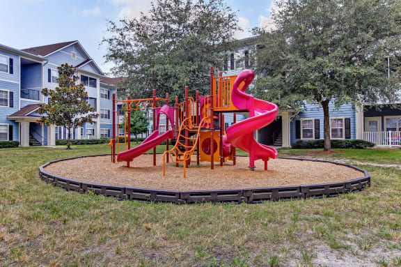 A playground with a red slide and orange climbing structure at Magnolia Village Apartments, Jacksonville, Florida