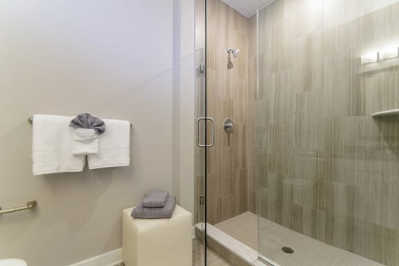 A bathroom with modern tile walls in a stand-up shower, a towel holder, and a stool with folded towels. at Keva Flats, Pennsylvania, 19341