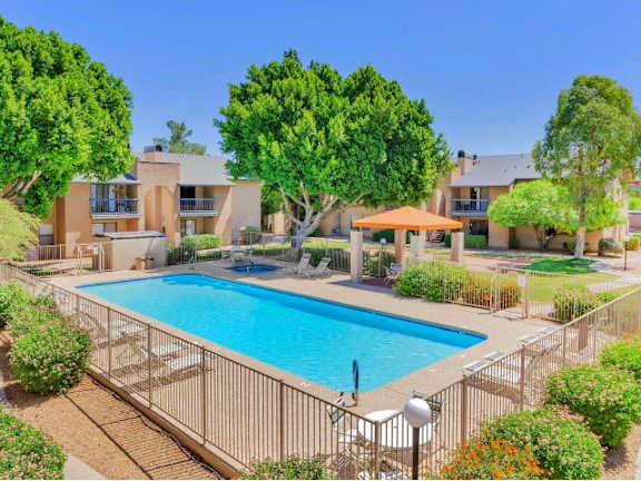 A large swimming pool surrounded by a fence and trees at Reflections at Red Mountain Apartments, Mesa 85213