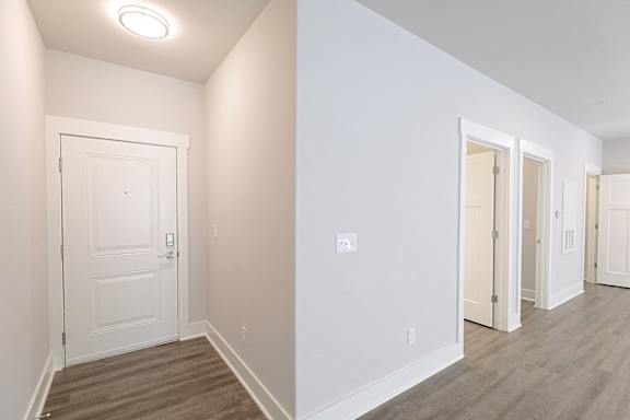 A white door is in a hallway with wood floors at McHenry Square Apartments, Augusta