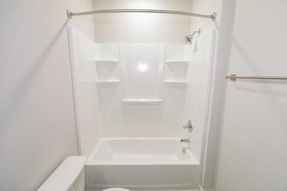 A white bathroom with a tub and shelves at McHenry Square Apartments, Georgia