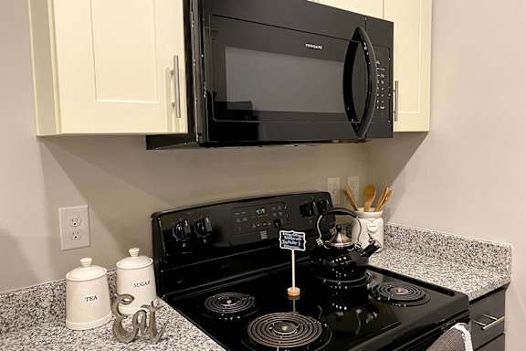 A black microwave oven is mounted above a black stove in a kitchen at McHenry Square Apartments, Augusta, GA