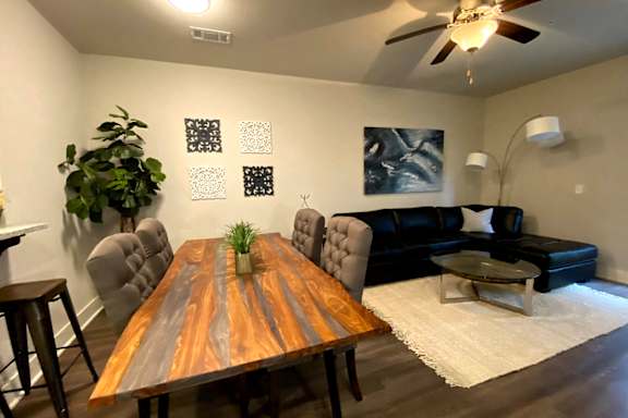 A wooden table with a plant on top is in the middle of a room with a black couch and a white rug at McHenry Square Apartments, Augusta, GA, 30909