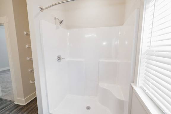 A white shower stall with a door and a shower head at McHenry Square Apartments, Georgia