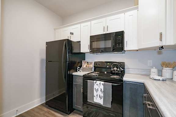 A black refrigerator and stove in a kitchen with white cabinets at McHenry Square Apartments, Augusta