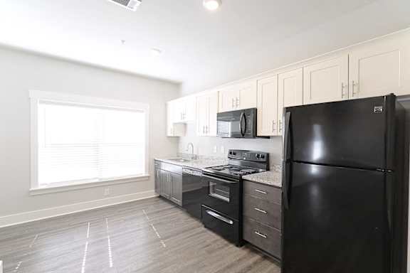 A black refrigerator is in a kitchen with white cabinets and a black stove at McHenry Square Apartments, Augusta, GA