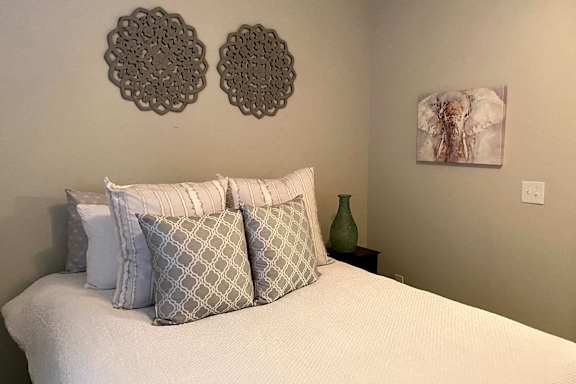 A bed with a white comforter and four pillows with a grey and white pattern at McHenry Square Apartments, Augusta, GA