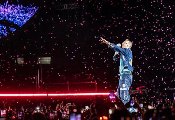 A person in a blue outfit is performing on stage with confetti falling from the sky.