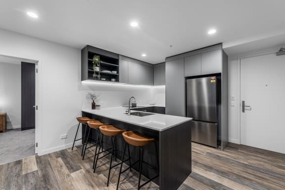 a kitchen with a large island with three stools and a stainless steel refrigerator
