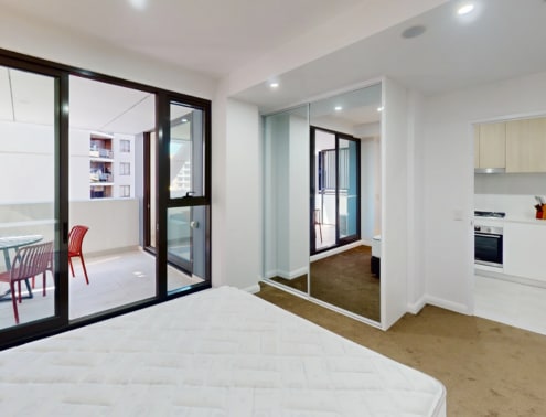 A bedroom with a large bed and a kitchen area in the background.