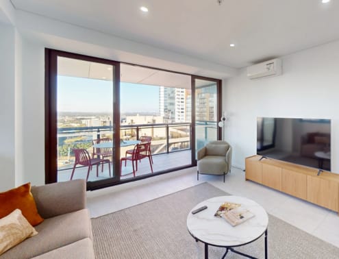 A living room with a grey couch, a coffee table, a television, and a balcony with chairs.