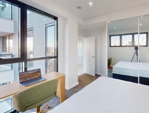 A room with a bed, a desk with a laptop, and a green chair.