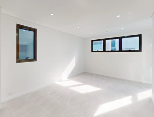A room with white walls and a tiled floor with sunlight streaming in through the windows.