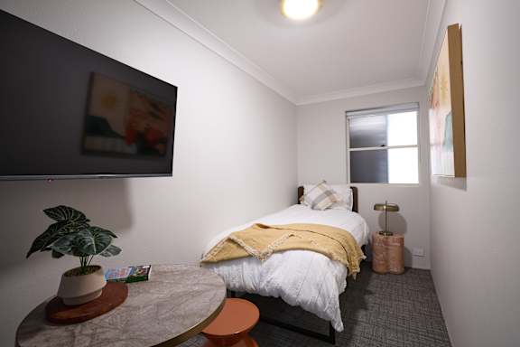 A bedroom with a bed, a small table, and a potted plant.