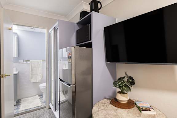 A bathroom with a refrigerator and a TV mounted on the wall.