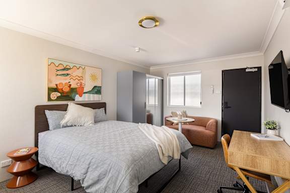 A bedroom with a bed, a chair, a table, and a painting on the wall.