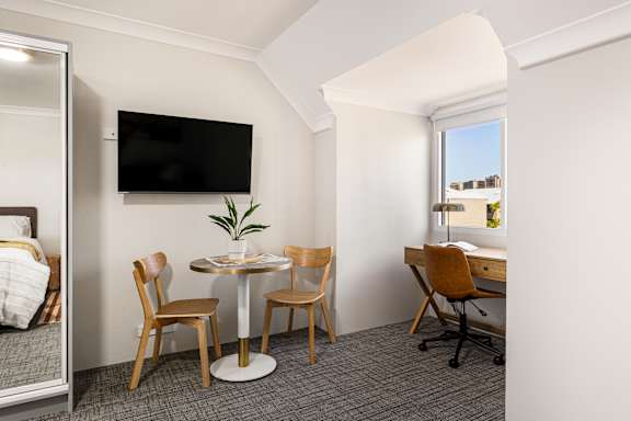 A room with a table, chairs, and a television mounted on the wall.