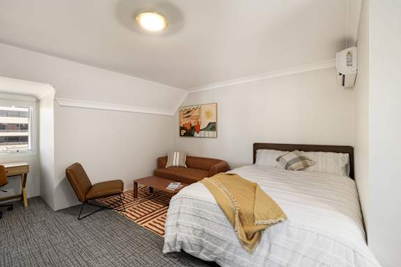 A bedroom with a bed, chair, and a painting on the wall.