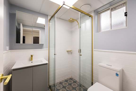 A bathroom with a white sink and a gold shower.