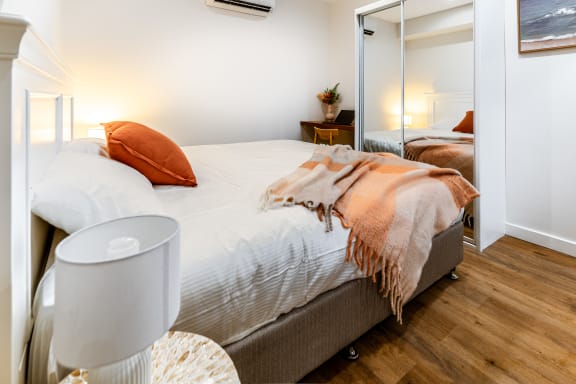 a bedroom with a bed with white sheets and orange pillows