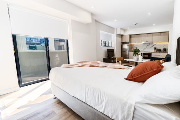 a bedroom with a large bed and a kitchen with a sliding glass door