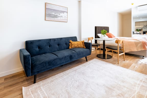 a living room with a blue couch and a table and a bed