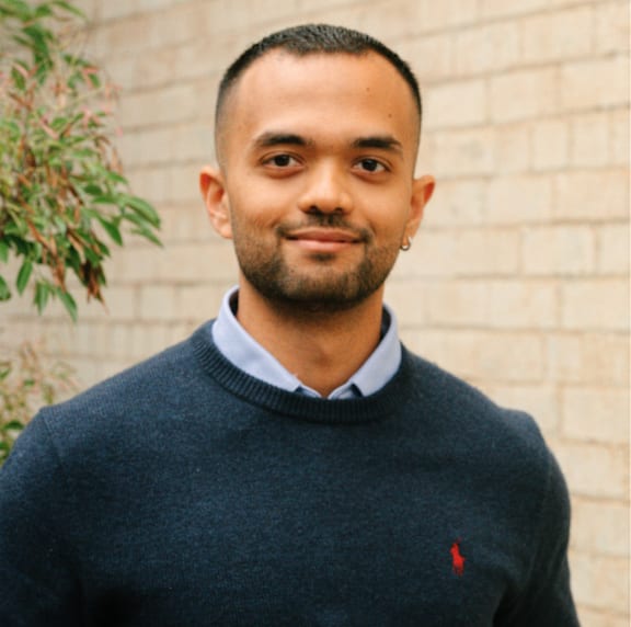 A man wearing a dark blue sweater with a small red logo on the left chest.