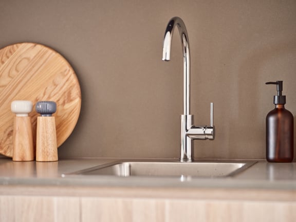 a kitchen sink with a silver faucet and a wooden cutting board