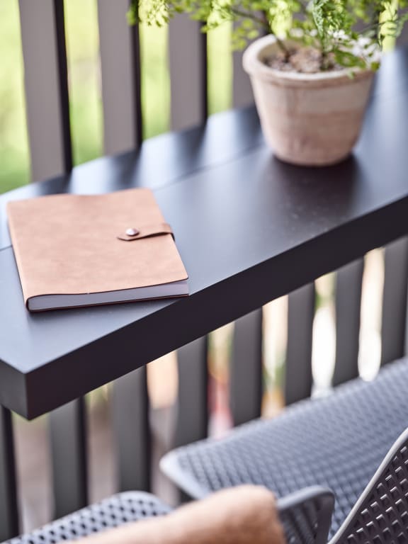 a table with a notebook and a chair with a plant on a balcony