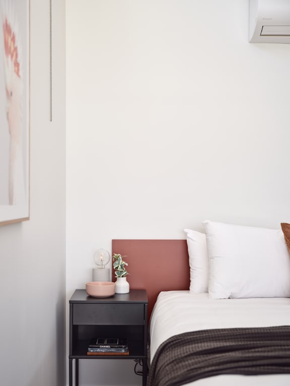 a bedroom with a bed and a nightstand with a pink plant on it