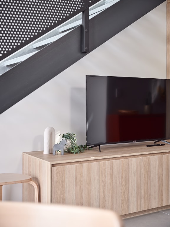 a tv on a wooden cabinet under a staircase in a living room