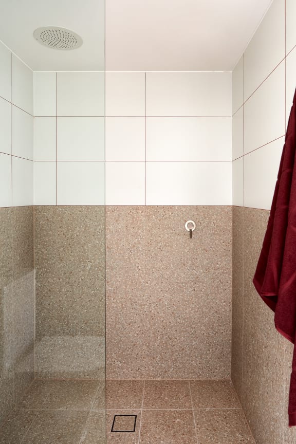 a shower with red towels in a white tiled bathroom