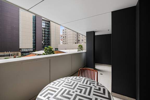 A black and white patterned couch sits in a room with a black wall and a window overlooking a cityscape.